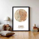 a framed map of Cairo, Egypt, with a stack of books and a lamp on a wooden floor in the foreground.