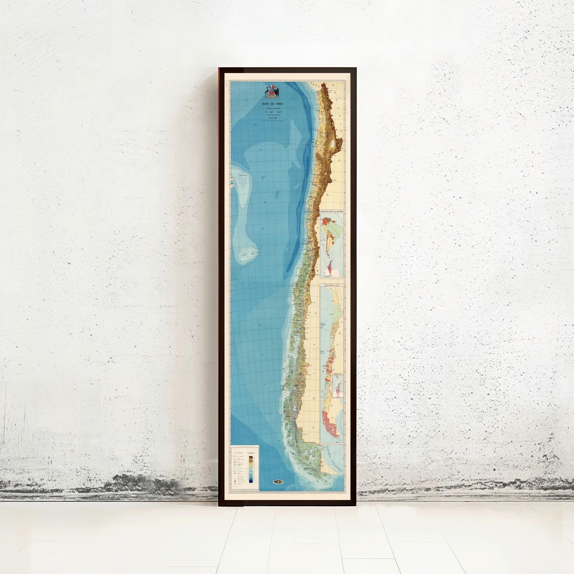 a tall, narrow framed map of South America, specifically Chile, standing against a white wall.