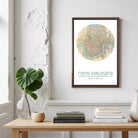 a framed map of New Orleans, with a potted plant, stack of books, and a vase on a wooden table below it.