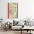 a living room with a large framed subway map hanging on the wall, a gray sofa with a stack of books, a wooden side table, and a vase with greenery.