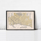 The image is a framed vintage map of a city, likely from the 19th century, displayed on a wall.