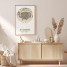 a wooden cabinet with a framed map of Antwerp, a city in Belgium, hanging on the wall above it. The cabinet is situated in a room with a beige color scheme, and there are decorative elements such as a potted plant, a vase, and a book on the cabinet.