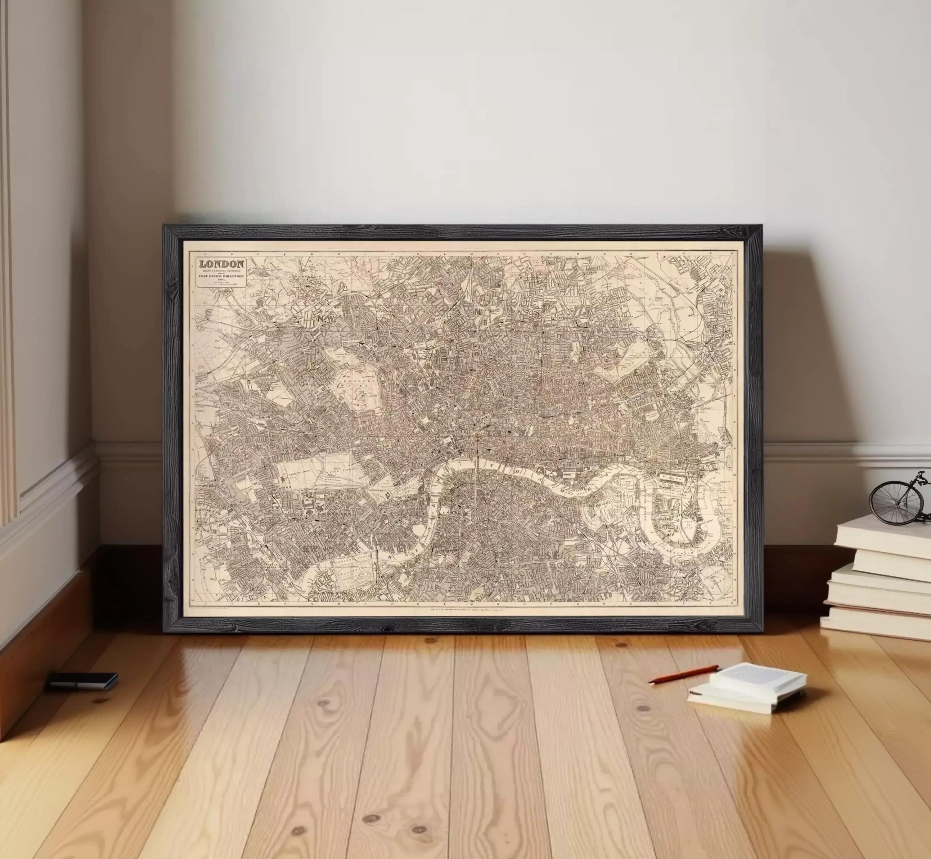 A framed map of London is displayed on a wooden floor, with a stack of books and a pen nearby.