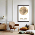 a living room with a framed map of Saint Louis, Missouri, hanging on the wall. The room has a beige armchair, a wooden side table, and a lamp. There are also some books and pillows on the floor, creating a cozy and inviting atmosphere.