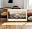 The image is a framed print depicting a landscape with a river, buildings, and trees.