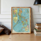 A framed vintage map of the Philippines is displayed on a wooden floor next to a stack of books.