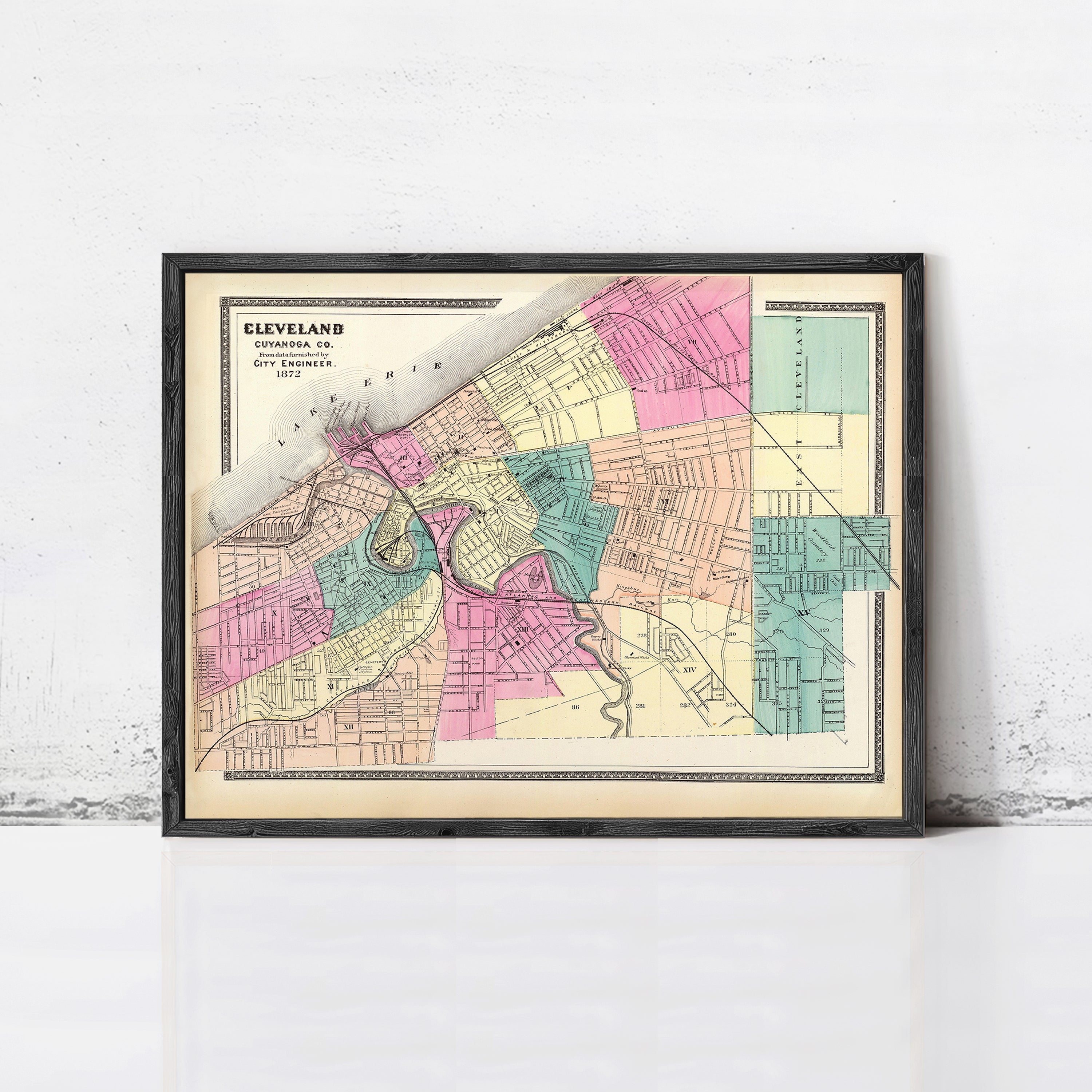 The image is a framed vintage map of Cleveland, Ohio, depicting the city's streets and neighborhoods in a colorful, detailed manner.