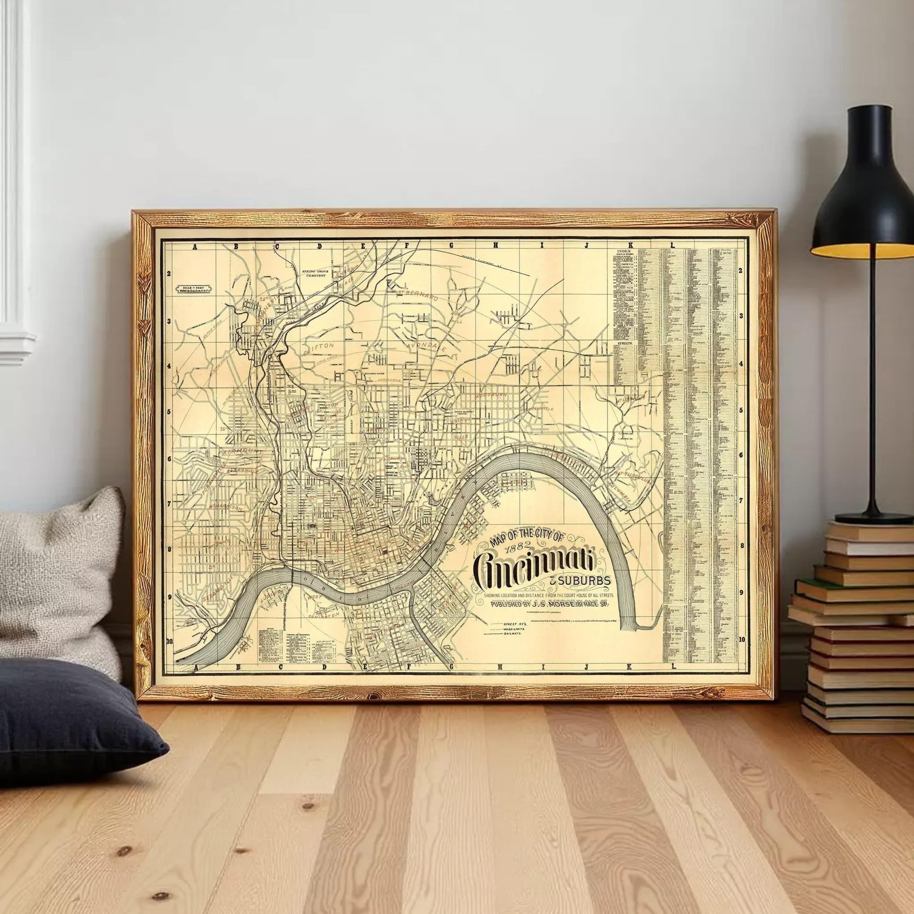 a large framed map of Cincinnati, Ohio, with a wooden frame and a black lamp on a wooden floor in the background.