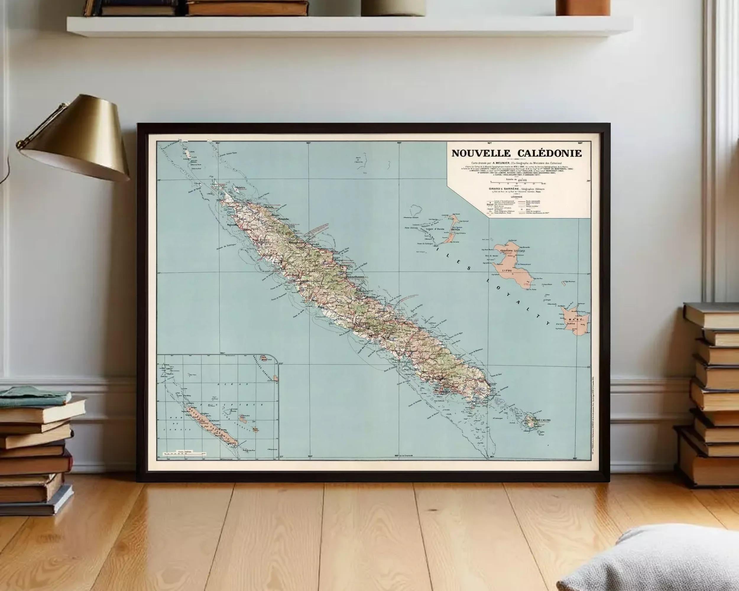 a framed vintage map of the island of Nueville, Caledonia, with a wooden floor and a bookshelf in the background.