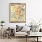 a living room with a large framed map of South America hanging on the wall above a couch with pillows. There are also some books and a vase with flowers on the couch, creating a cozy and inviting atmosphere.