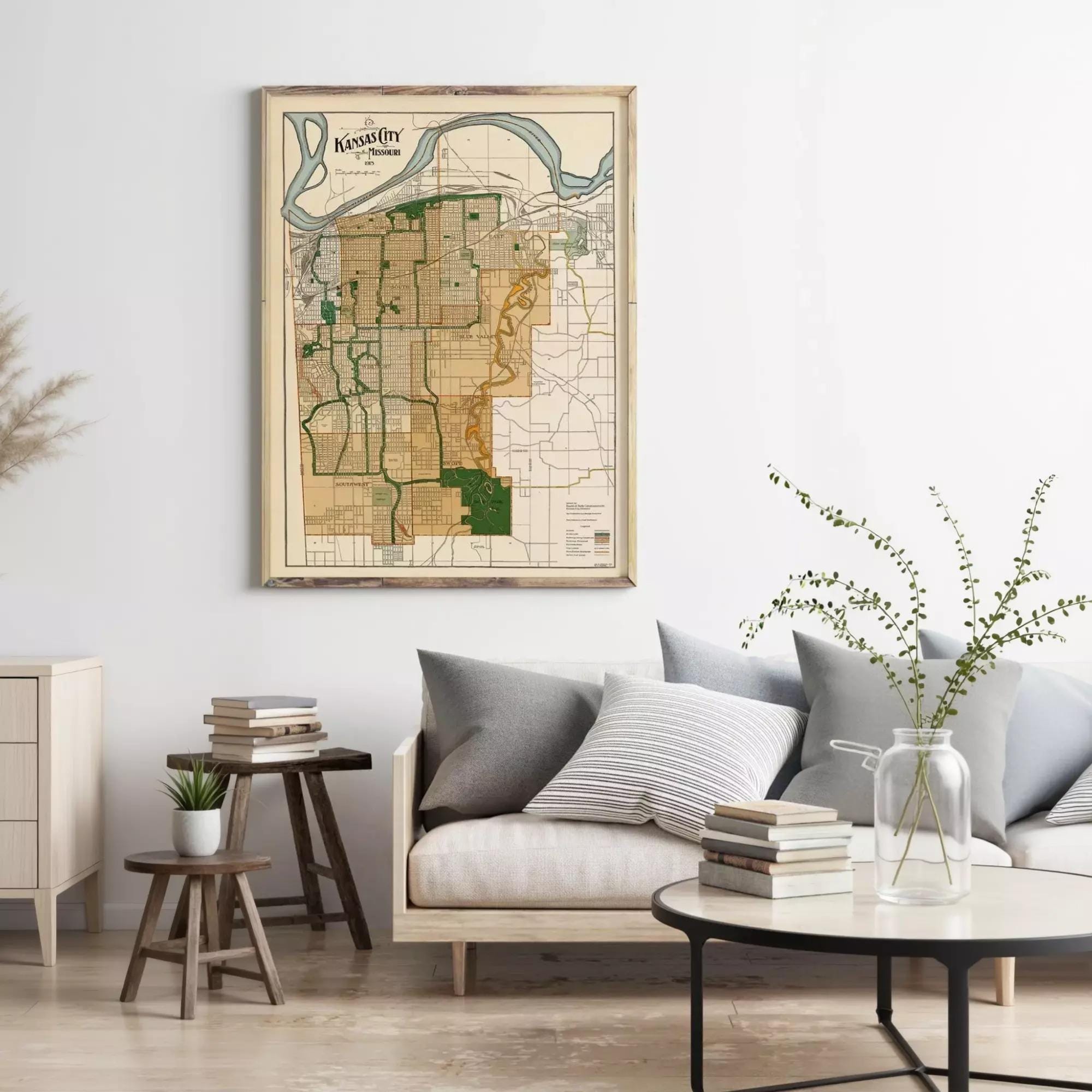 a living room with a framed map of Kansas hanging on the wall above a couch with pillows. There are also some books and a vase on a table in the room.