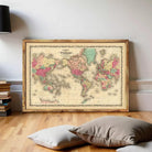 The image is a vintage world map in a wooden frame, displayed on a white wall.
