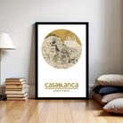 a framed poster of a map of Casablanca, with a stack of books and a lamp to the left of the frame.