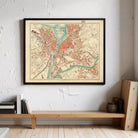 a framed map of a city hanging on a wall, with a wooden bench and some books below it.