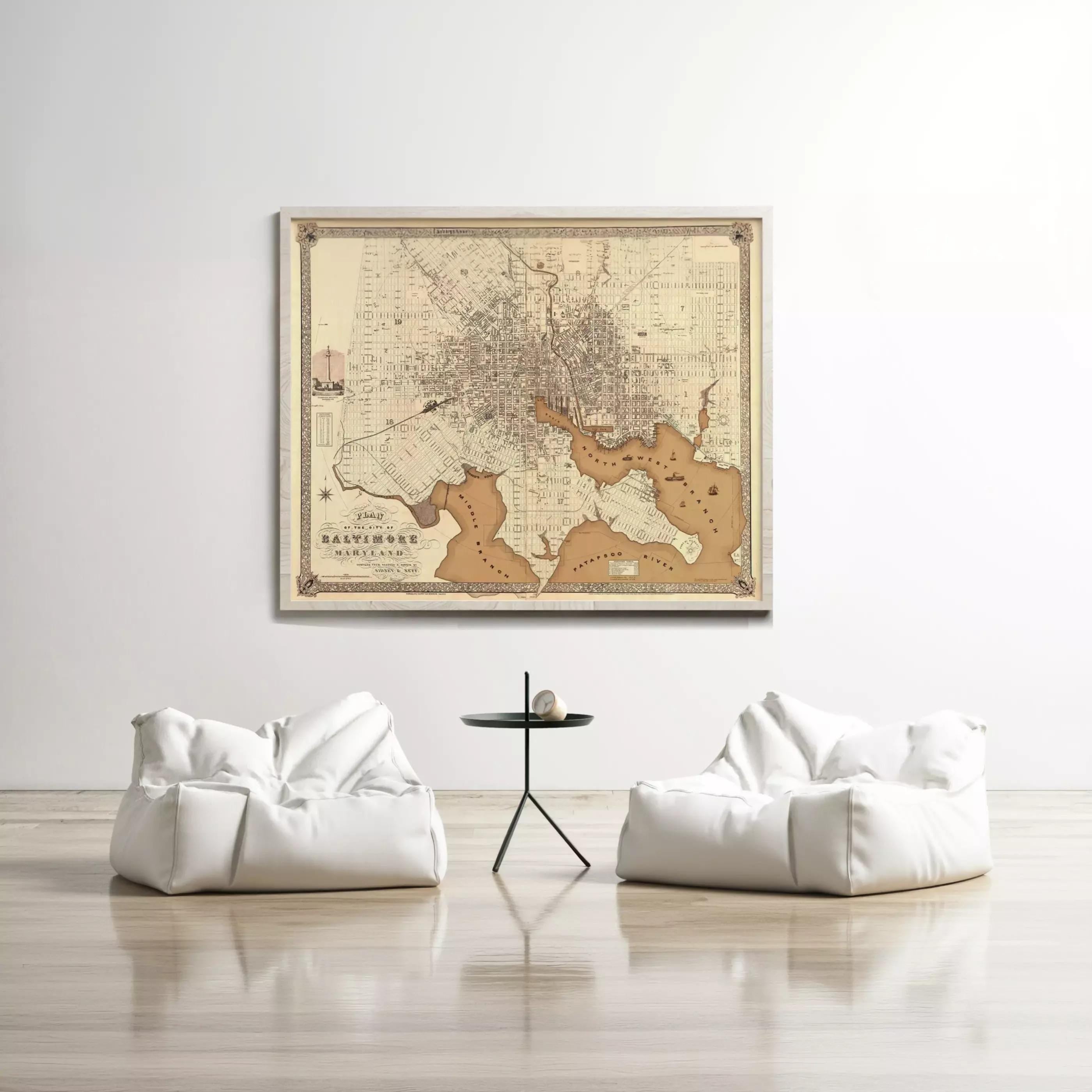a large framed map of Baltimore, Maryland, hanging on a white wall above two white bean bag chairs and a small black table.
