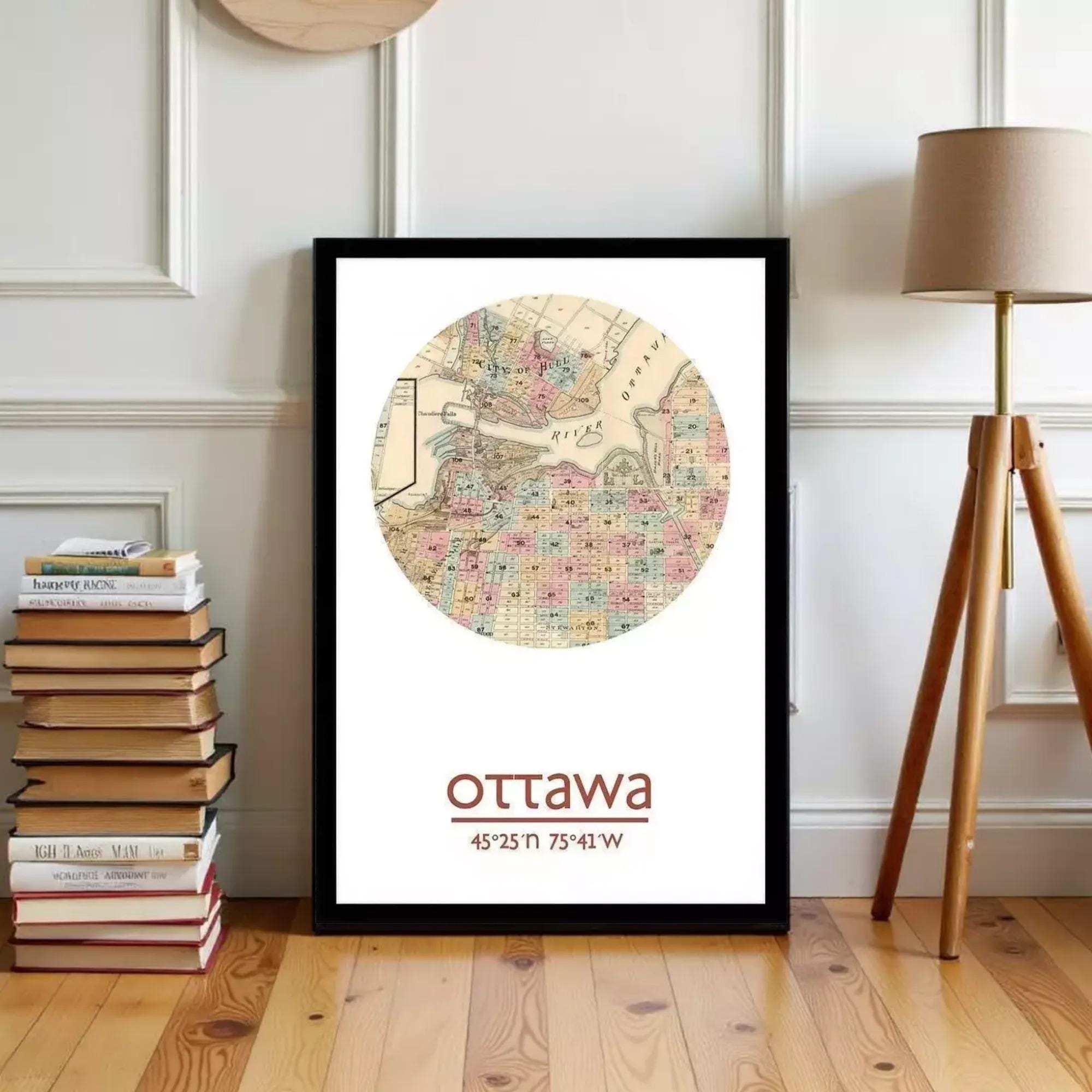 A framed map of Ottawa, Canada, with the city's name and location printed on it, is displayed on a wooden floor next to a stack of books and a lamp.