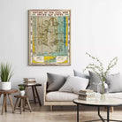 a living room with a large framed map of the United States hanging on the wall, a couch with pillows, a coffee table with books and a vase of greenery, and a small table with a plant.