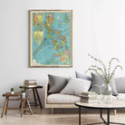 a living room with a large framed map of the Philippines hanging on the wall above a gray sofa with striped pillows. The room also includes a coffee table with a vase of greenery, a stack of books, and a small side table with a plant.