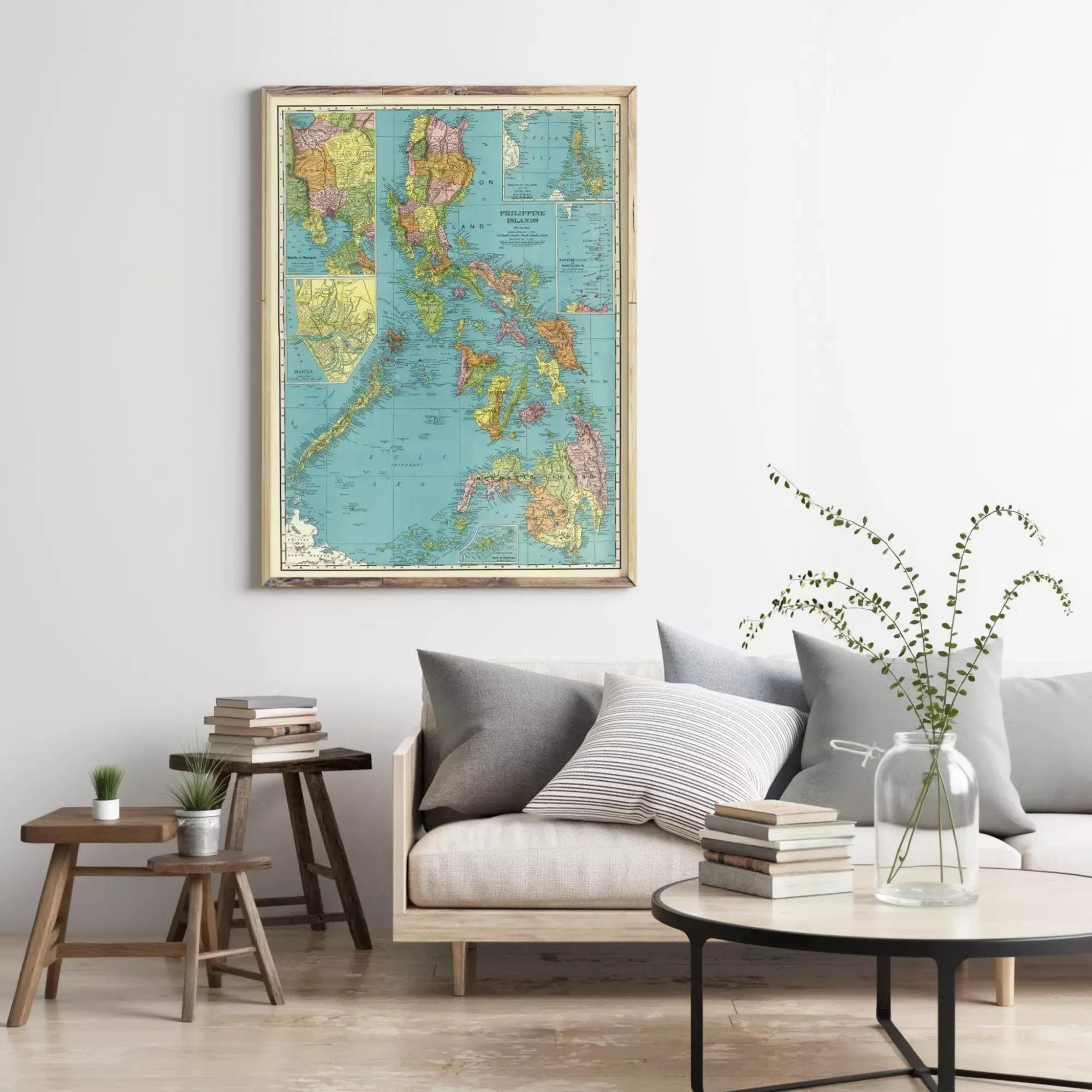 a living room with a large framed map of the Philippines hanging on the wall above a gray sofa with striped pillows. The room also includes a coffee table with a vase of greenery, a stack of books, and a small side table with a plant.