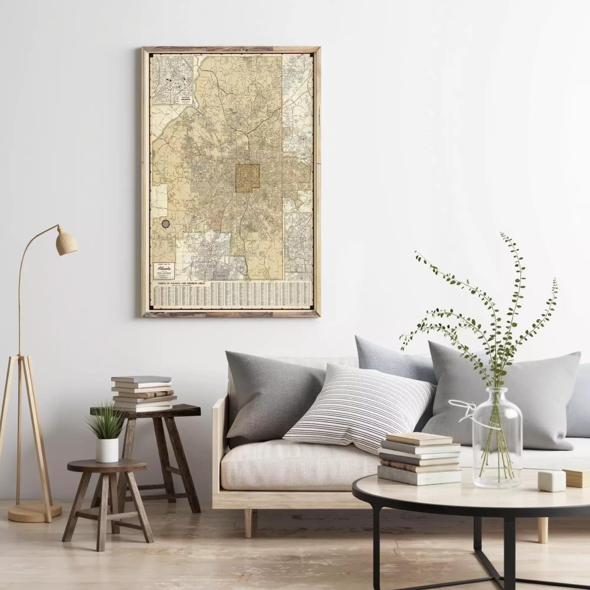 a cozy living room with a large framed map hanging on the wall, a comfortable gray sofa with striped pillows, a wooden side table with a plant, and a round coffee table with books and a vase of greenery.