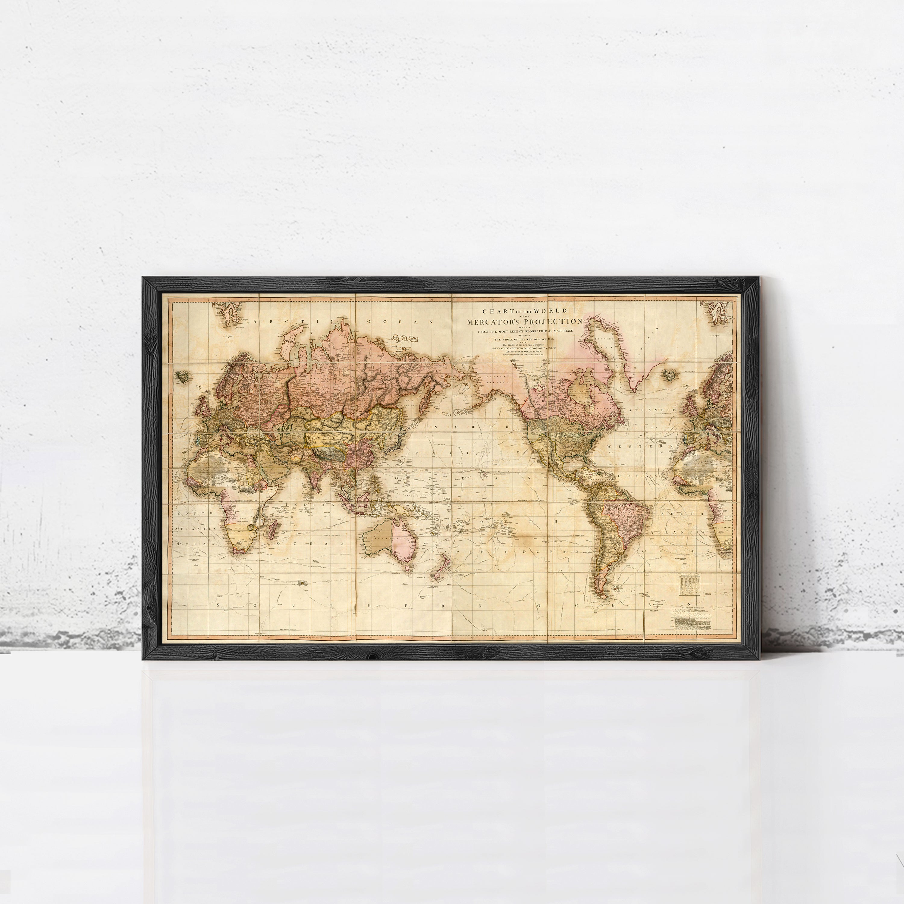 The image is a framed vintage world map with a black border, displayed on a white wall.