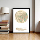 A framed map of Kansas City, with the city's location and surrounding area, is displayed on a wall next to a stack of books and a lamp.