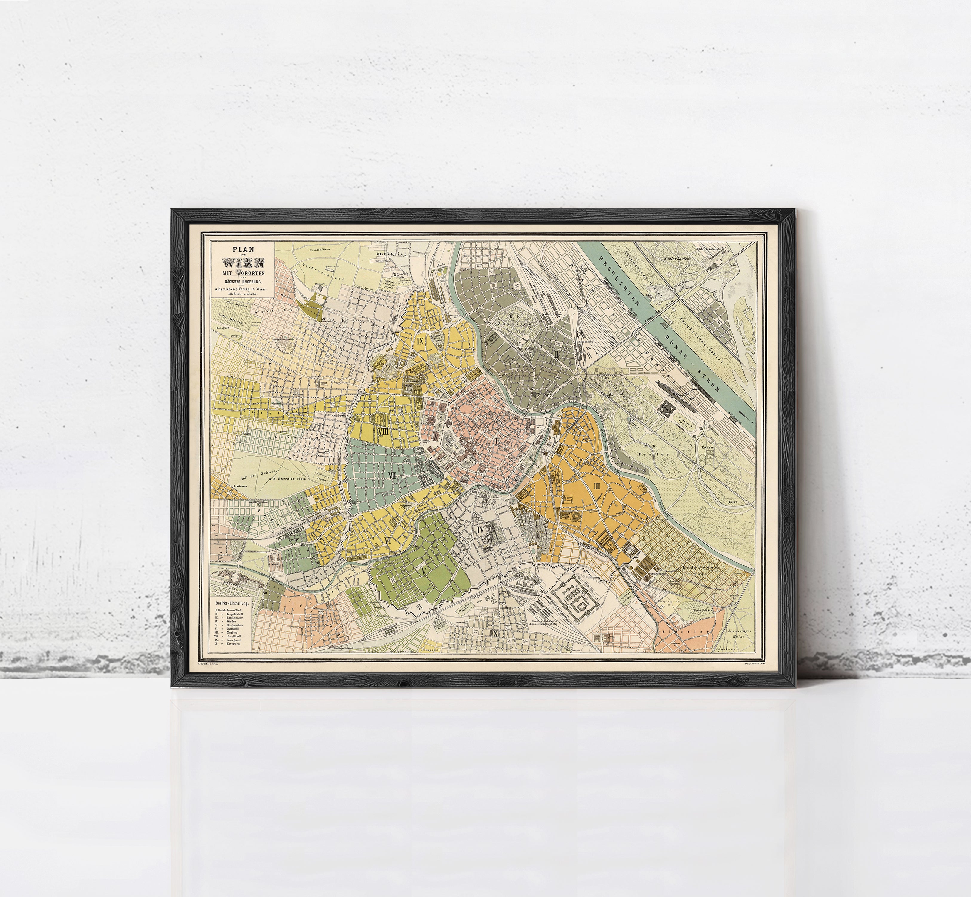 The image is a framed vintage map of a city, likely from the 19th century, displayed on a wall.