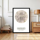 a framed map of Dresden, Germany, with a wooden dresser and a stack of books visible in the background.