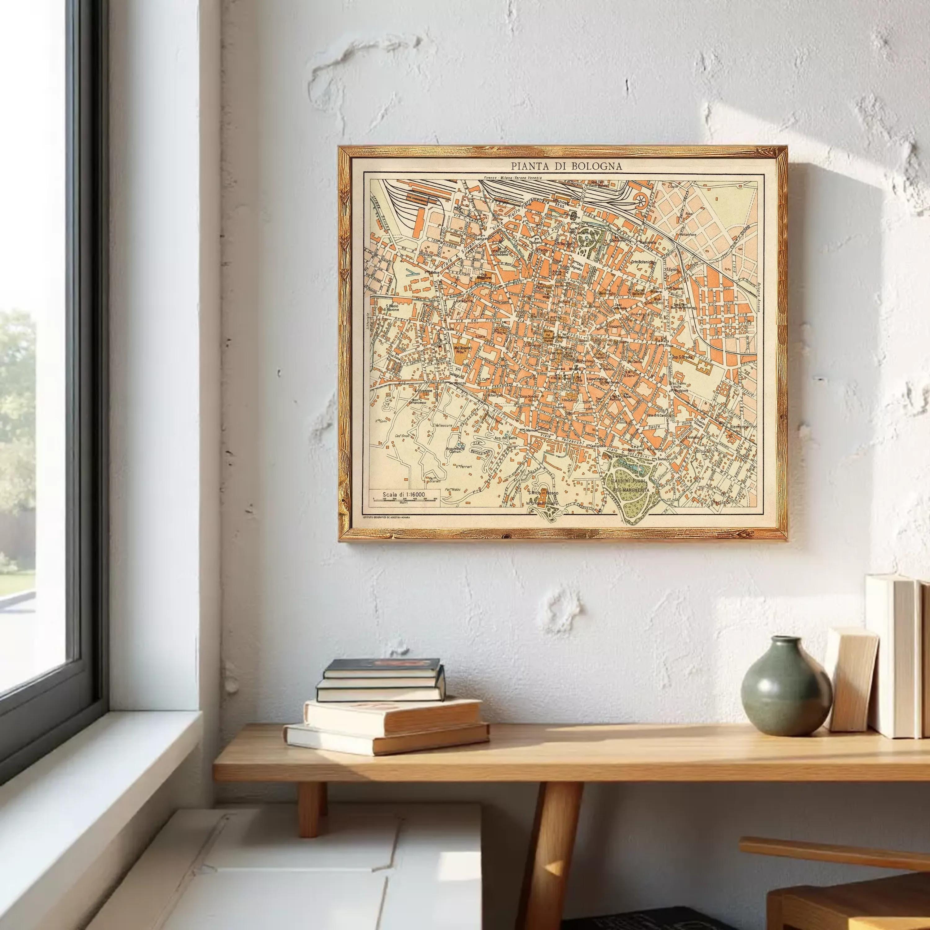 a framed map of a city hanging on a wall, with a wooden table below it and some books and a vase on the table.