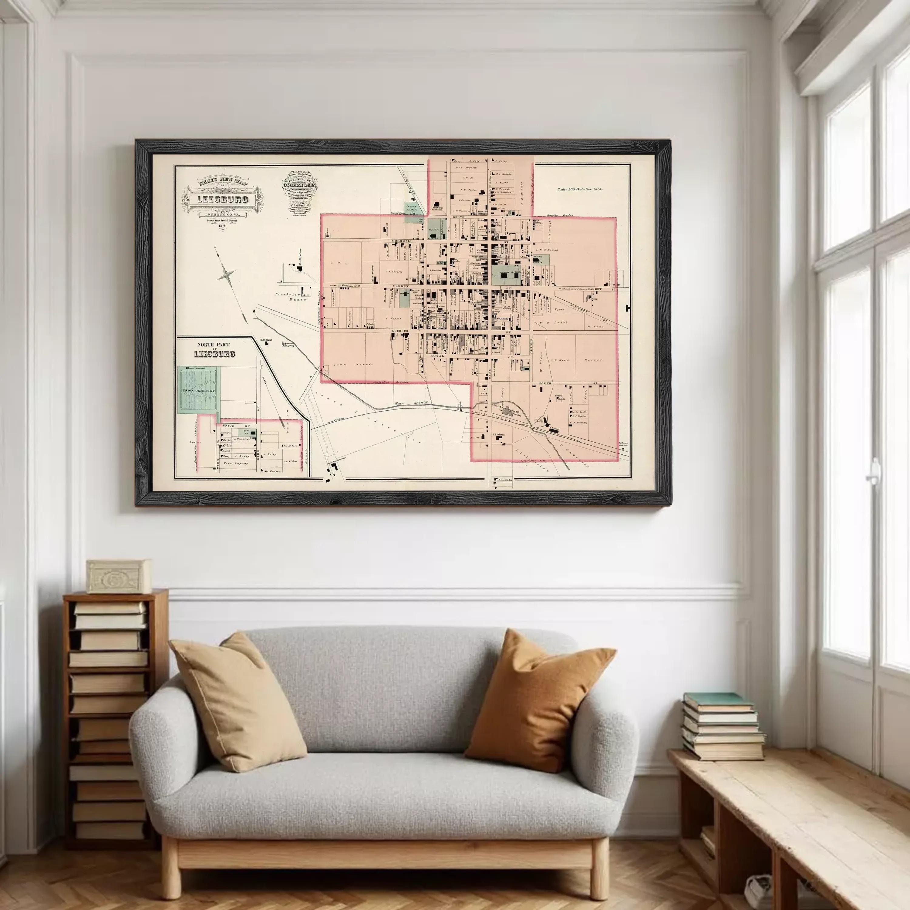 a large framed map of a city hanging on a wall above a gray sofa with two pillows.