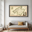 a large framed map of the Mediterranean region hanging on a wall above a gray sofa with a single yellow throw pillow.