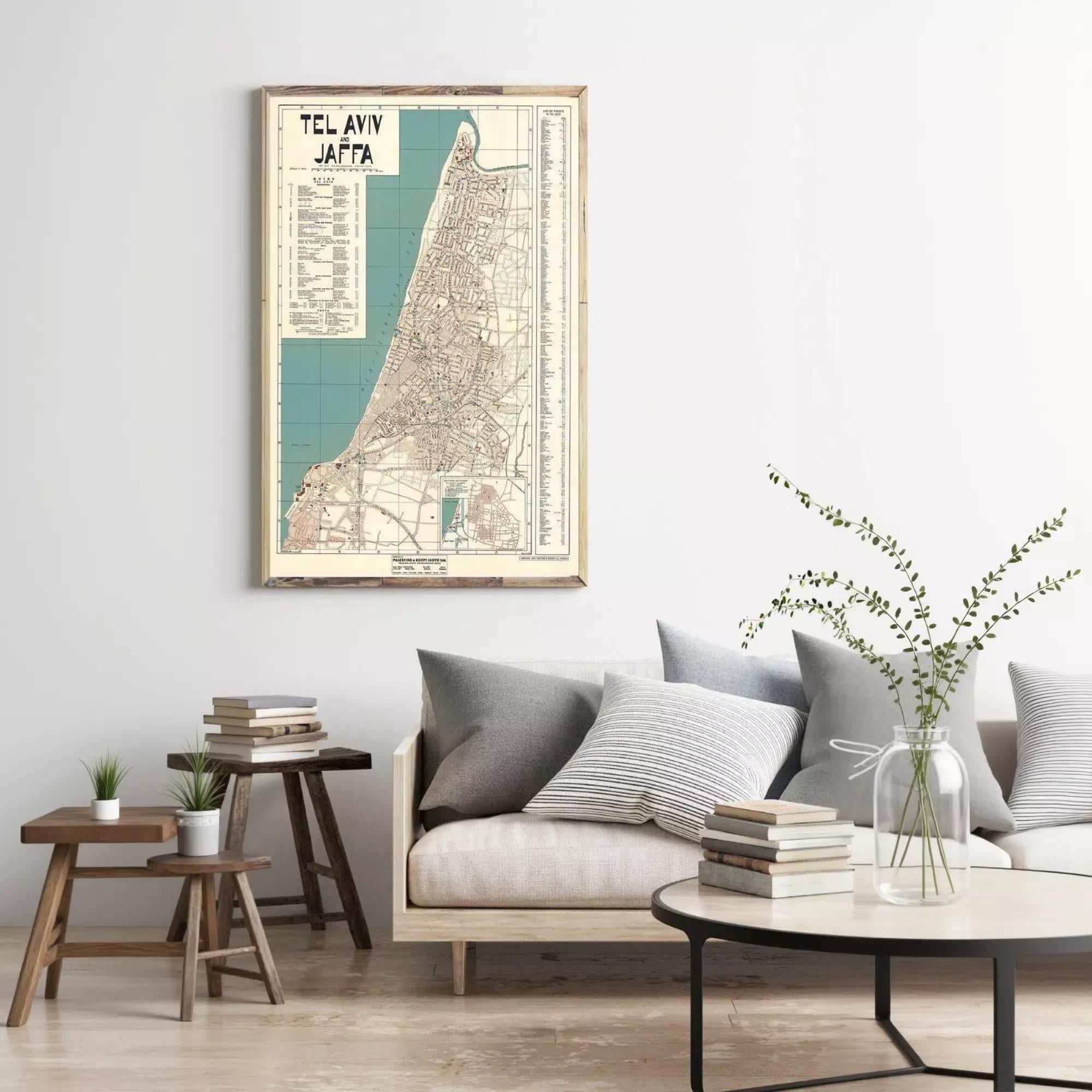 a living room with a framed vintage map of Tel Aviv, Israel, hanging on the wall above a couch with pillows. The room also includes a coffee table with books and a vase of greenery, creating a cozy and inviting atmosphere.