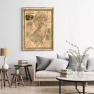 a living room with a large framed map of New Jersey hanging on the wall above a couch with pillows. The room also includes a coffee table with books and a vase of greenery.