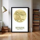 A framed map of Iceland, with the name " Reykjavik" printed on it, is displayed on a wall in a room with a lamp and a stack of books.