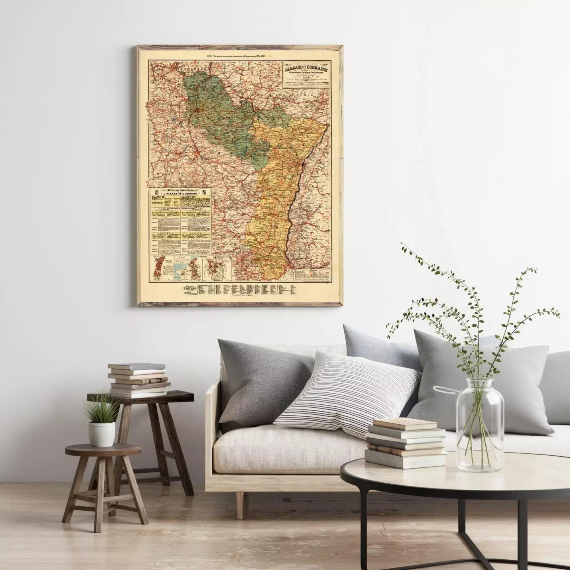 a living room with a large framed map hanging on the wall, a couch with pillows, a coffee table with books and a vase of greenery, and a small wooden stool.