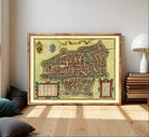 The image is a framed antique map of a city, likely from the Middle Ages, with intricate details and a decorative border.