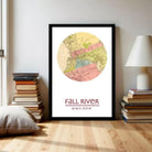 A framed map of the fall river is displayed on a wall, with a stack of books and a lamp to the side.
