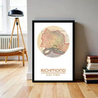 A framed map of Richmond, Virginia, with the city's name and location printed on it, is displayed on a wall in a room with a lamp and bookshelf in the background.