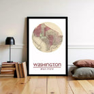 A framed map of Washington, D.C., with the city's location and coordinates displayed, is hanging on a wall next to a stack of books and a lamp.