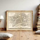 a large framed map of a city, with a wooden floor and a stack of books in the background.