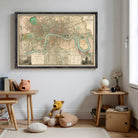 a framed map of London hanging on a wall, with a teddy bear sitting on the floor in front of it.