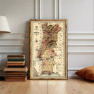 A framed map of Portugal is displayed on a wall, surrounded by a stack of books and a lamp.