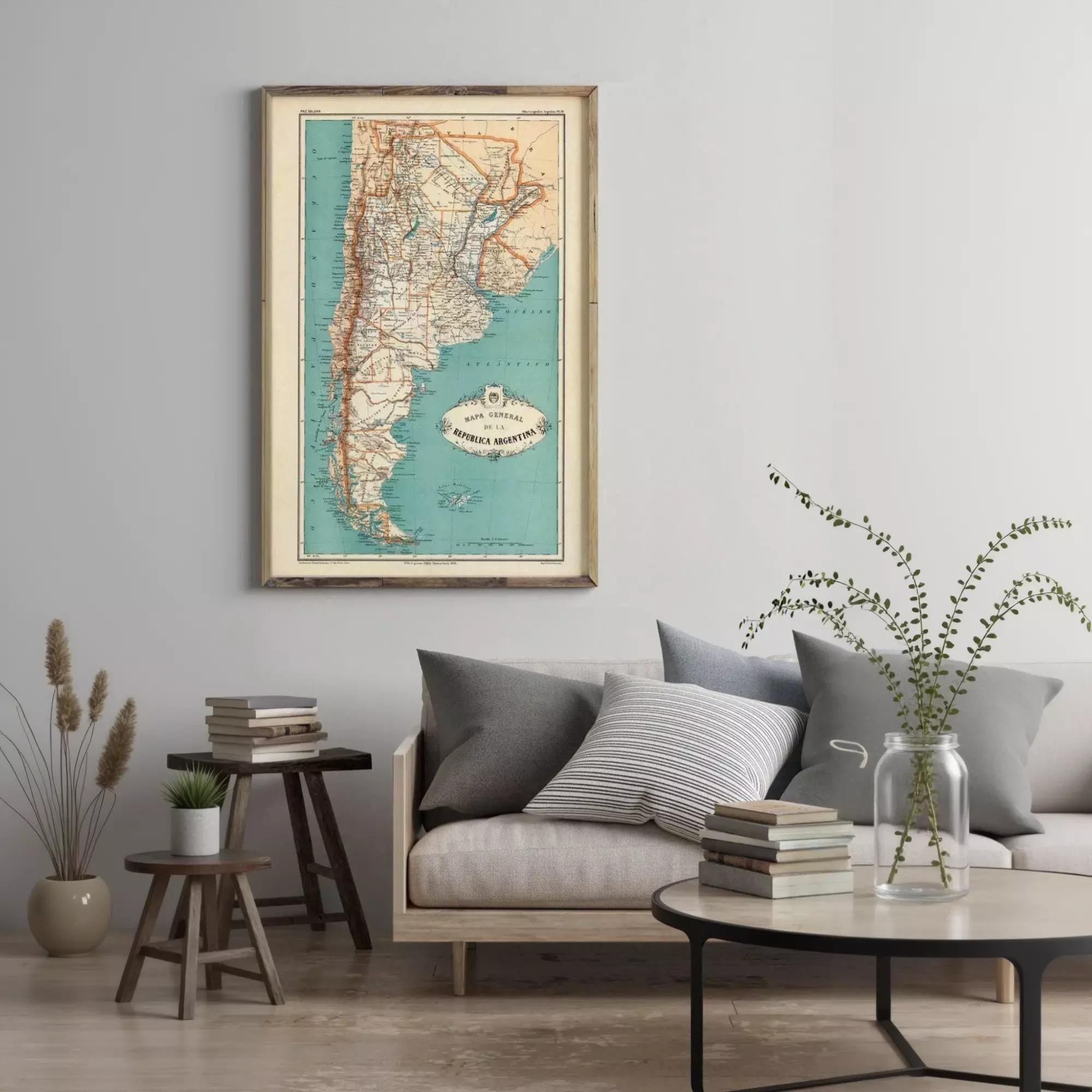 a living room with a framed map of Argentina hanging on the wall above a couch with pillows. There are also some books and a vase on the coffee table in front of the couch.