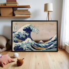 The image is a framed print of the famous Japanese woodblock print "The Great Wave off Kanagawa" by the artist Hokusai. The print depicts a large, powerful wave crashing against a rocky shore, with the wave's crest towering over the surrounding landscape. The artwork is framed in a black frame and is displayed on a white wall.