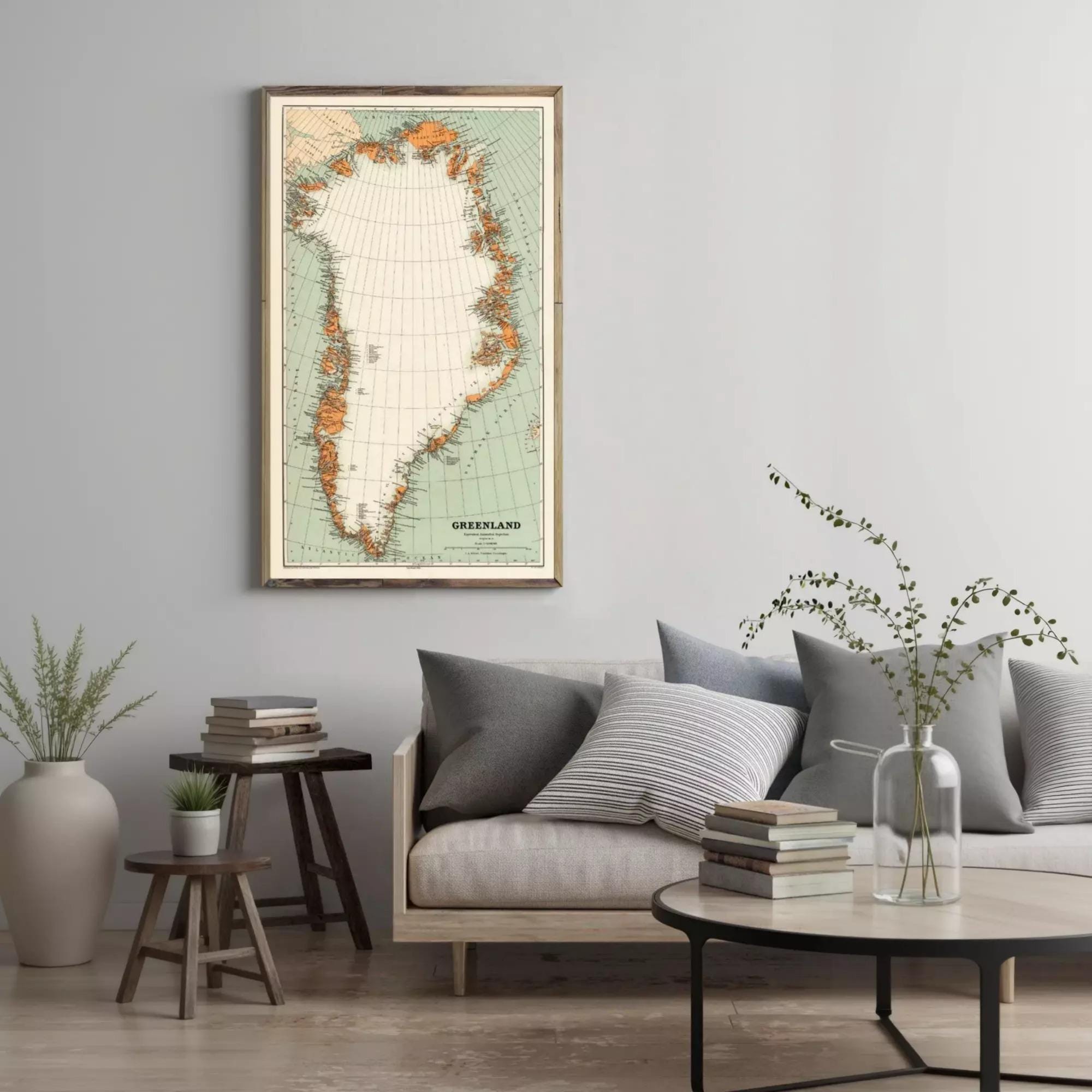 a living room with a large map of Greenland hanging on the wall. The room has a gray sofa, a wooden side table, and a round coffee table with books and a vase of greenery.