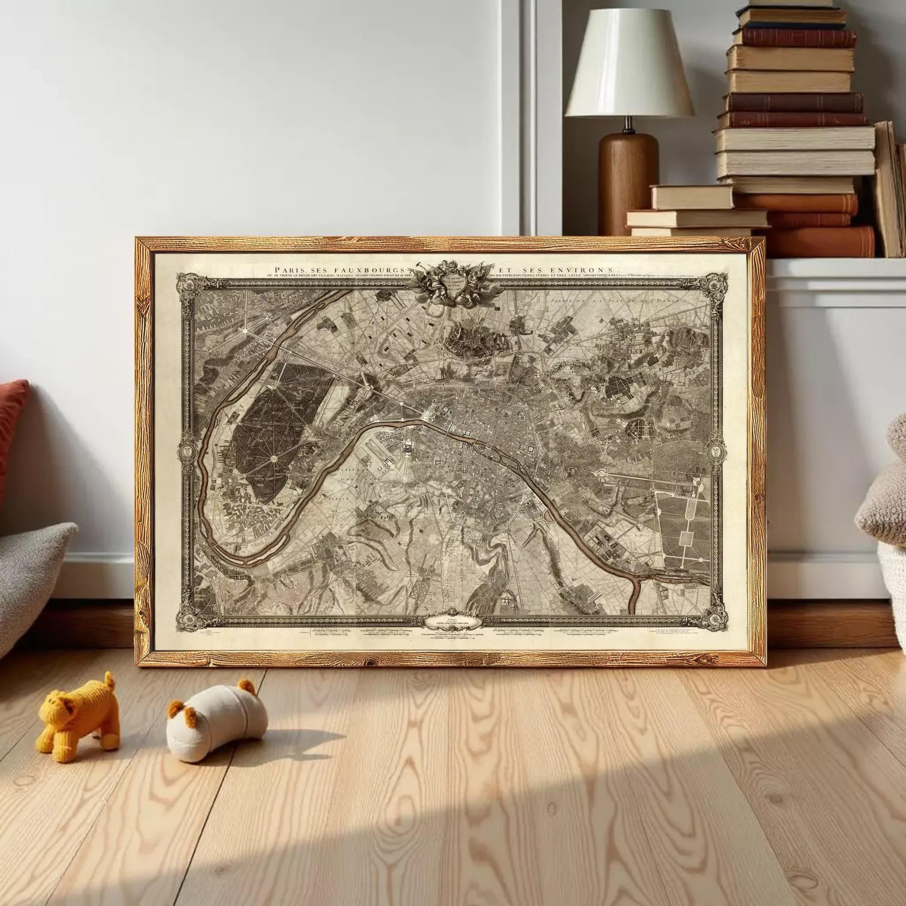 A framed map of Paris, France, displayed on a wooden floor in a room with a lamp and bookshelf in the background.