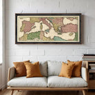 A framed vintage map of Europe and the Mediterranean region hangs on a white brick wall above a white couch with orange throw pillows.