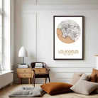 a living room with a framed map of Los Angeles hanging on the wall. The room has a minimalist and modern design, with a wooden chair, a lamp, and a stack of books on a table.